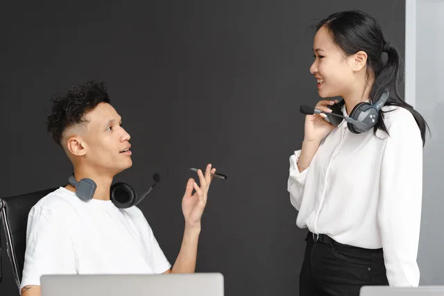 Two colleagues with headsets chat in a modern office setting, emphasizing teamwork and communication. Choosing when a chat should become a support ticket