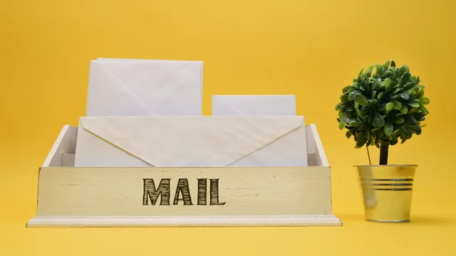 A wooden mail organizer with white envelopes and small potted plant on a yellow background. Connecting email inboxes to a shared support system