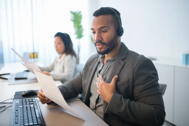 Businessman working at a call center desk, wearing a headset and reading documents. Designing ticket statuses around resolution work