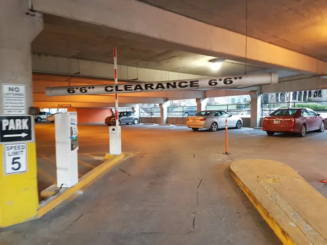 Parking barrier gate with arm raised to the vertical open position, allowing vehicle access through a controlled parking lane. Same installation type as typical commercial parking access control. Support platform access