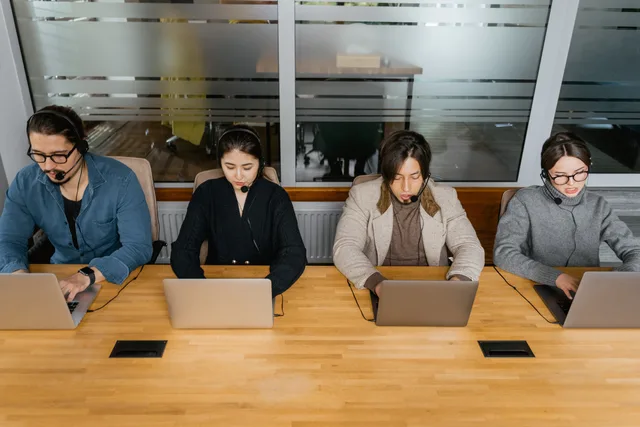 Group of diverse employees in headsets working on laptops in a modern office space. Support workforce tools