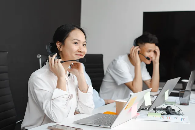 A diverse group of call center agents working with laptops and headsets in a modern office. Ticket management systems